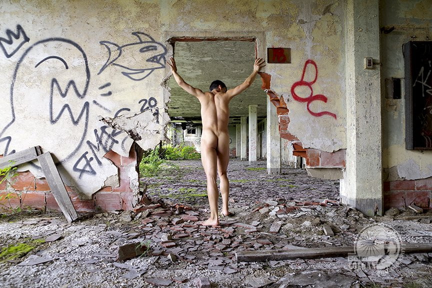 Nude man from behind with arms holding up remaining doorway in abandoned building