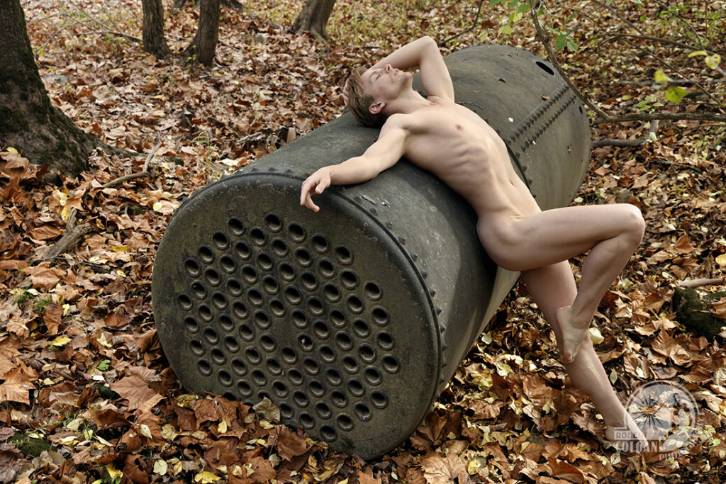 nude man laying across old rusty boiler in woods