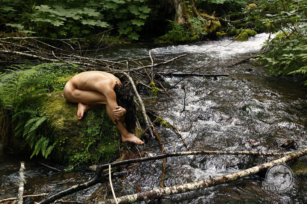 nude man on mossy rock in stream