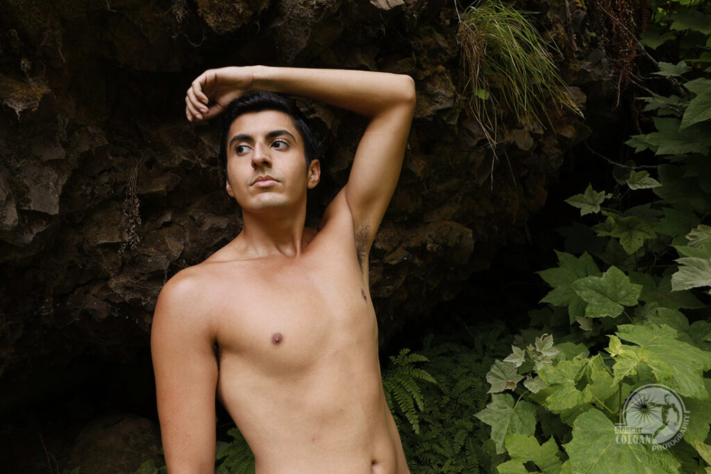 shirtless man stands beside wooded cliff