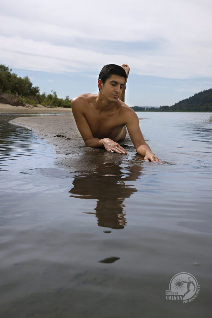 nude man lays on sand bar in river