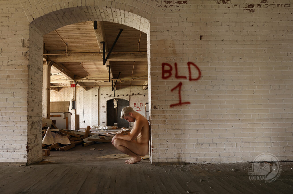 nude man squats in a doorway between rooms in an abandoned building