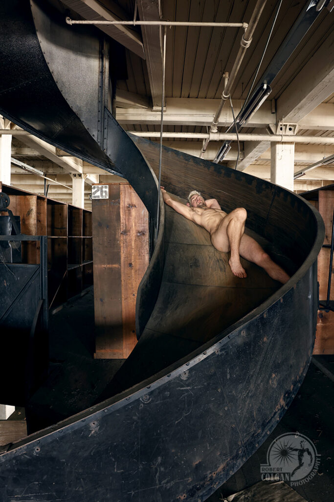 nude man on a spiral metal slide in an old warehouse