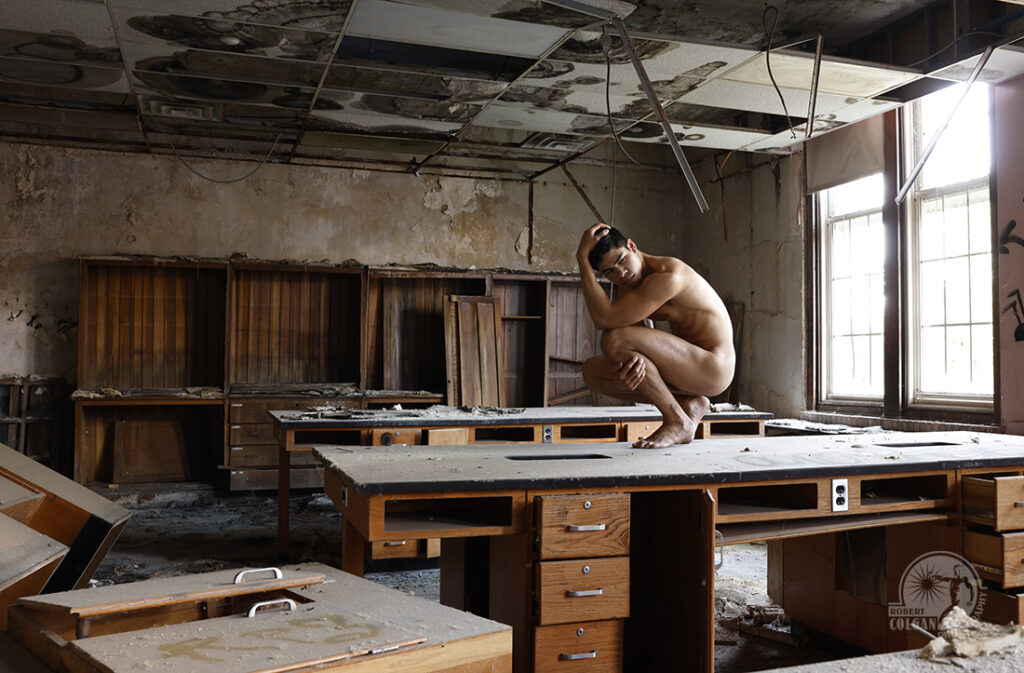 nude man in fetal position on work tables in ruined chemistry lab