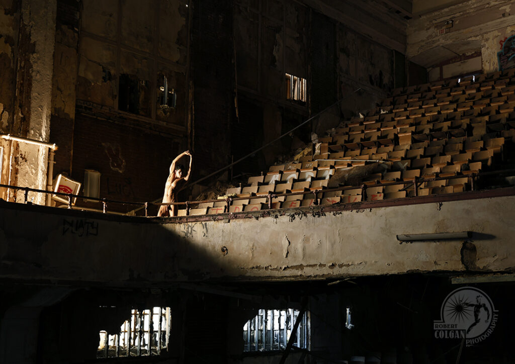 nude man stretches in light coming throiugh doorway of old theatre