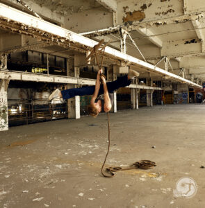 aerialist practices hanging from rope in empty factory