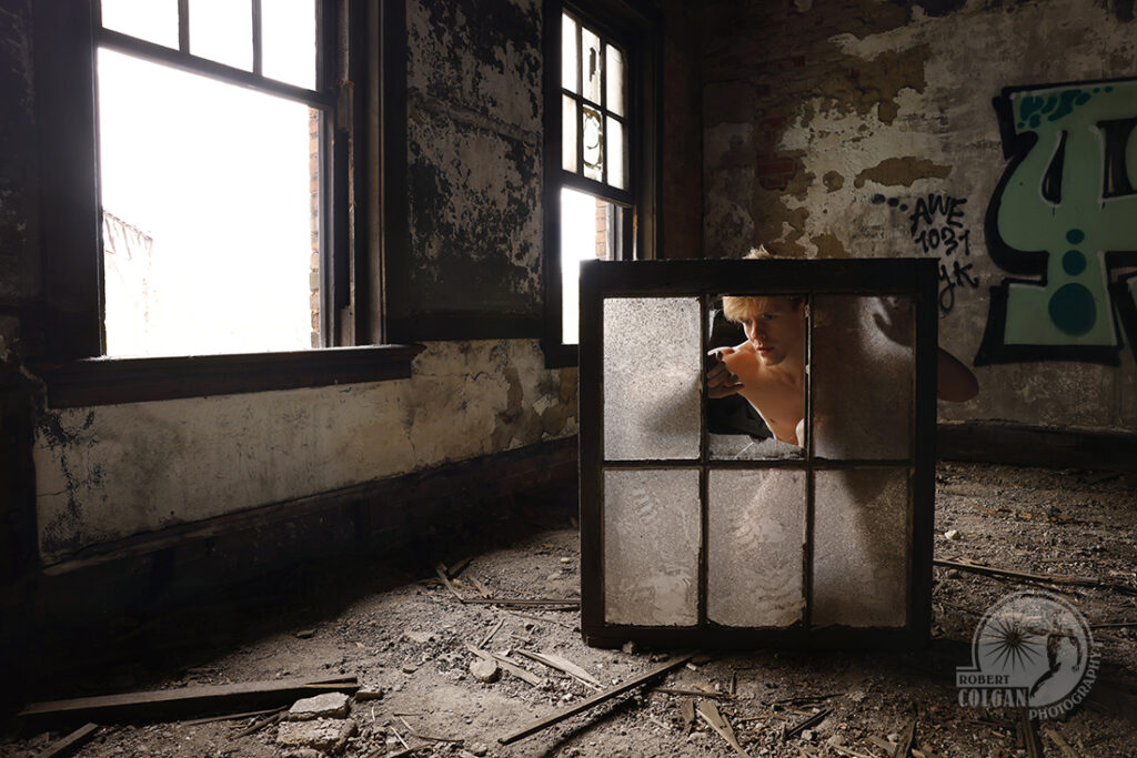 nude peers from behind broken window frame in dark old building