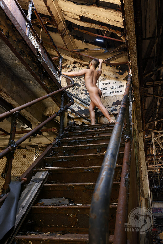 nude man in stretch pose at top of stairs