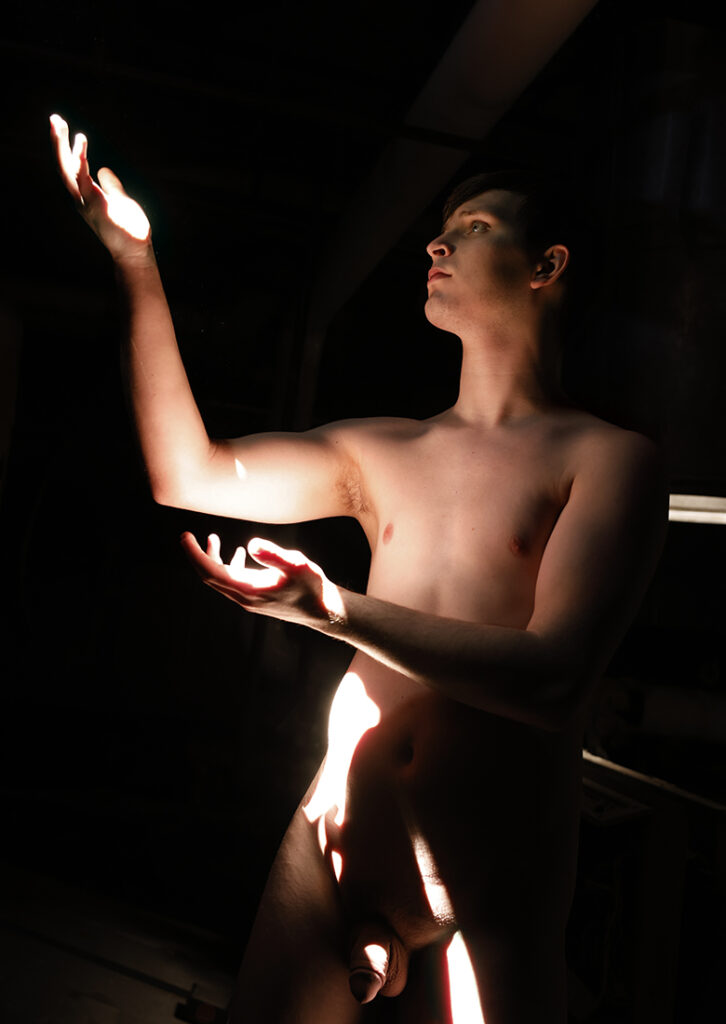 nude man in darkened room gestures toward sunbeam