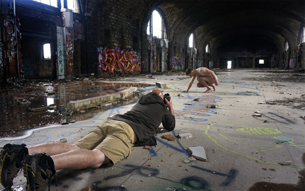 photographer lying on ground of old building with model posing in front of him