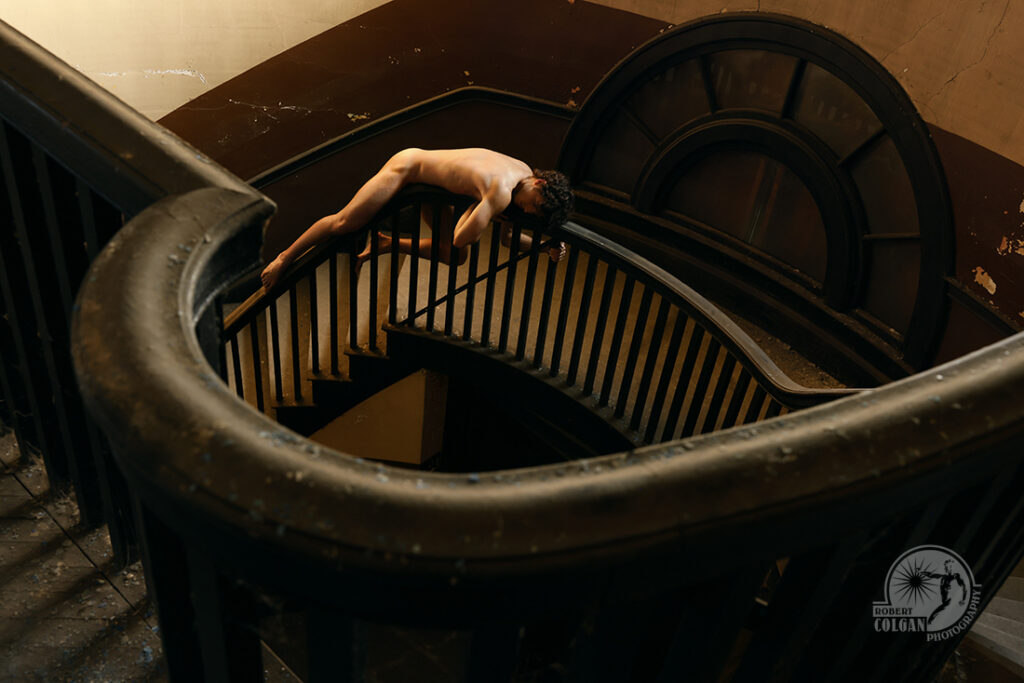 nude man lays precariously on the railing of a curvaceous stairway